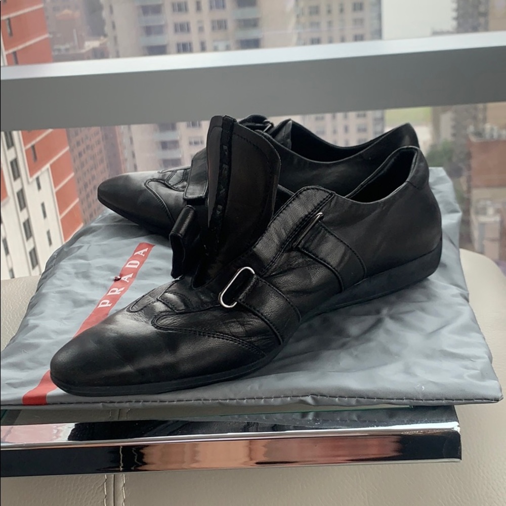 Black leather pointed closed toe Prada sneakers.